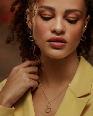 The 14K Solid Gold Geometric Minimal Necklace from the Harmony Collection features a thin chain adorned with two interlinked, irregularly shaped open circle pendants made of real solid yellow gold. This minimalist and elegant design is hypoallergenic and crafted using sustainable methods.