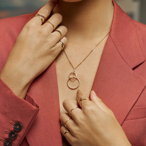 The 14K Solid Gold Geometric Intertwined Round Circles Necklace from the Harmony Collection showcases two elegantly linked circular pendants, delicately suspended from a fine chain and meticulously handcrafted using sustainable methods.