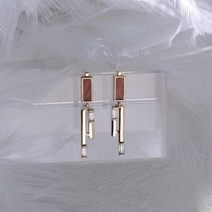 A pair of earrings from the Achates Collection made of 14K solid gold, showcasing rectangular orange agate or carnelian gemstones at the top, accented with hexagonal gold designs and small rectangular clear gemstones below.