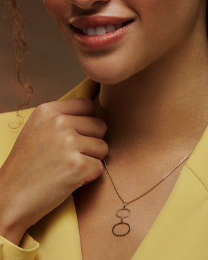 The 14K Solid Gold Geometric Minimal Necklace from the Harmony Collection features a thin chain adorned with two interlinked, irregularly shaped open circle pendants made of real solid yellow gold. This minimalist and elegant design is hypoallergenic and crafted using sustainable methods.