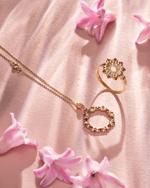 The Flower Ledder Ruby Pendant Necklace from the Chloris Collection showcases a circular pendant embellished with small lab-grown ruby accents and a delicate bow, intricately crafted from hypoallergenic 14K solid gold.