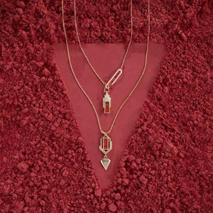 Introducing the Achates Collection: a 14K solid gold necklace with a geometric pendant that boasts vertical elements of orange and yellow gold. This elegant piece is accented by a natural carnelian gemstone, while an elongated link above the pendant provides a modern flair to its design.
