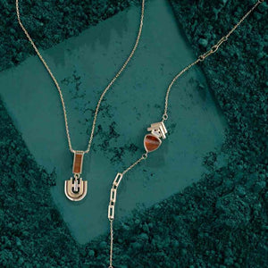 Part of the Achates Collection, this 14K solid gold necklace features a delicate chain with an oval pendant set with a small orange carnelian gemstone and an intricate geometric design below it. The pendant beautifully reflects light against a plain white background.