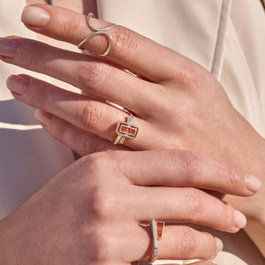 Introducing the Achates Collection: a 14K solid gold ring featuring a rectangular natural carnelian gemstone at its center, elegantly accented with small clear gemstones on each side. The band offers a simple yet sophisticated design.