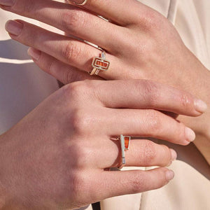 This 14K solid gold ring from the Achates Collection features a modern geometric design, showcasing an orange rectangular carnelian gemstone and a small clear gemstone set into its band. The contemporary style is highlighted by clean lines.