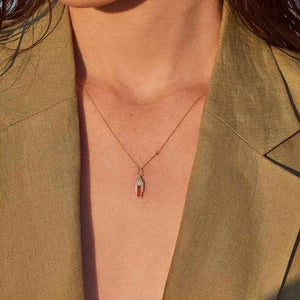 Introducing the Achates Collection: a 14K solid gold necklace with a geometric pendant that boasts vertical elements of orange and yellow gold. This elegant piece is accented by a natural carnelian gemstone, while an elongated link above the pendant provides a modern flair to its design.
