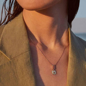 Part of the Achates Collection, this 14K solid gold necklace features a delicate chain with an oval pendant set with a small orange carnelian gemstone and an intricate geometric design below it. The pendant beautifully reflects light against a plain white background.