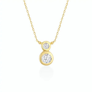 The 14K Gold Zirconia Necklace showcases two round diamond pendants on a delicate chain, arranged vertically with the larger pendant positioned below the smaller one. The white background enhances the necklace's elegance, making it an ideal piece of dainty gold jewelry for bridal occasions.