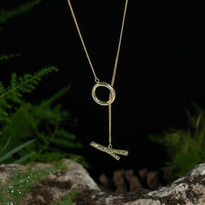 The 14K Solid Gold Tree Branch with O-Ring Necklace from the Into the Woods Collection by Erdem Akan showcases an elegant and minimalist design, featuring a circular loop and a delicate chain that ends in a pendant shaped like two intertwined twigs. This hypoallergenic necklace is available in multiple chain sizes.