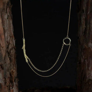 Introducing the 14K Solid Gold Tree Branch in Balance Necklace from the "Into the Woods" Collection by Erdem Akan. This exquisite piece features two distinct chain styles seamlessly connected to a textured branch-like element on one side and a smooth circular loop on the other. Made with sustainable practices, this necklace provides both elegance and peace of mind as it casts a subtle shadow against a white backdrop.