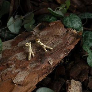 The 14K Solid Gold Tree Branch Stud Earrings from the Into the Woods Collection by Erdem Akan are expertly crafted to resemble small tree branches and are showcased on a white background. Made from authentic 14K solid gold, they feature a textured surface, are hypoallergenic, and designed for pierced ears with visible posts and backings.