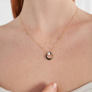 The necklace from the Elegance Collection is made of 14K solid yellow gold and features a circular pendant with a black accent and a natural pearl at its center. The hypoallergenic chain is delicate and enhances the elegant design of the pendant.