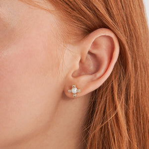 The 14K Solid Gold Theia Diamond Natural Pearl Dot Stud Earrings from the Elegance Collection feature a central pearl encircled by four gold prongs, each embellished with small lab-grown diamonds, creating a cross-like design. Crafted from hypoallergenic 14K real solid gold, one earring is displayed from the front and the other from the back.