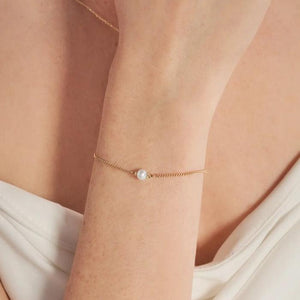 Introducing the 14K Solid Gold Natural Pearl Bracelet from the Elegance Collection: a refined chain bracelet crafted from delicate 14K solid gold, showcasing a single natural pearl at its center. It features an adjustable clasp and includes a small gold tag for fastening.