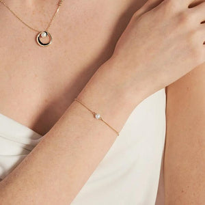 Introducing the 14K Solid Gold Natural Pearl Bracelet from the Elegance Collection: a refined chain bracelet crafted from delicate 14K solid gold, showcasing a single natural pearl at its center. It features an adjustable clasp and includes a small gold tag for fastening.