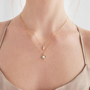 Part of the Elegance Collection, the 14K Solid Gold Natural Pearl Double Layer Necklace features a hypoallergenic design with two layers: the upper chain displays a small diamond-shaped pendant while the lower chain highlights an intricate intertwined design holding a natural pearl, all set against a white background.