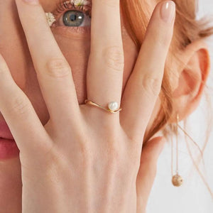 The 14K Solid Gold Natural Pearl Ring from the Elegance Collection showcases a minimalist design with a single real pearl gracefully set at its center. The band features a smooth, modern twist, emphasizing the pearl against a simple white backdrop, and is crafted using sustainable methods.