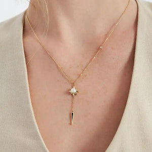 The 14K Solid Gold Natural Pearl Necklace from the Elegance Collection showcases a star-shaped pendant with a natural pearl at its center. It is attached to a long chain that ends in a black pointed charm, accented by a small crystal above the star, all set against a plain white background.