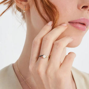 The 14K Solid Gold Natural Pearl Ring from the Elegance Collection boasts a natural pearl set against a white backdrop, enhanced by a modern and elegant design featuring a black accent along the band, all crafted with sustainable methods.