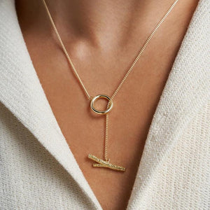 The 14K Solid Gold Tree Branch with O-Ring Necklace from the Into the Woods Collection by Erdem Akan showcases an elegant and minimalist design, featuring a circular loop and a delicate chain that ends in a pendant shaped like two intertwined twigs. This hypoallergenic necklace is available in multiple chain sizes.