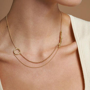 Introducing the 14K Solid Gold Tree Branch in Balance Necklace from the "Into the Woods" Collection by Erdem Akan. This exquisite piece features two distinct chain styles seamlessly connected to a textured branch-like element on one side and a smooth circular loop on the other. Made with sustainable practices, this necklace provides both elegance and peace of mind as it casts a subtle shadow against a white backdrop.