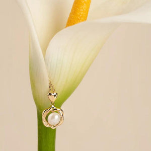 The 14K Solid Gold Natural Pearl Necklace from the Elegance Collection showcases a gold necklace with a delicate chain, featuring a heart-shaped link that holds a circular pendant. The pendant is designed with an intricate knot pattern encircling a single natural pearl. Crafted from real 14K solid yellow gold, this piece has a polished, hypoallergenic, and elegant appearance.