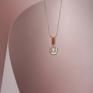 Part of the Achates Collection, this 14K solid gold necklace features a delicate chain with an oval pendant set with a small orange carnelian gemstone and an intricate geometric design below it. The pendant beautifully reflects light against a plain white background.