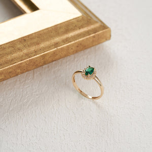 This 14K solid gold ring, named the Emerald May Birthstone Ring, features an oval green gemstone surrounded by dazzling diamonds, capturing a vintage aesthetic. The hallmark is gracefully engraved inside its smooth band.