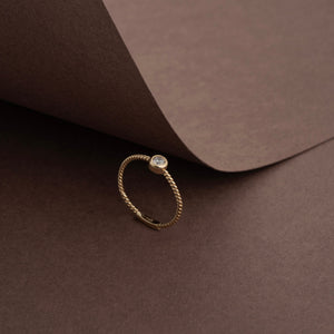 A refined 14K solid gold ring showcases a minimalist rope design and features a central round diamond in a bezel setting. Set against a plain white background, it exudes both elegance and simplicity.