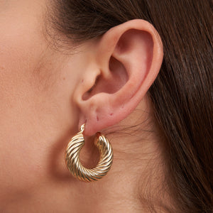 The two earrings on display are the 14K Real Hold Thick Twist Rope Hoops, showcasing a chunky design crafted from 14K gold. They feature a shiny finish with a clasp closure engraved with RUND A NIX, and are presented with one earring front-facing and the other side-facing.