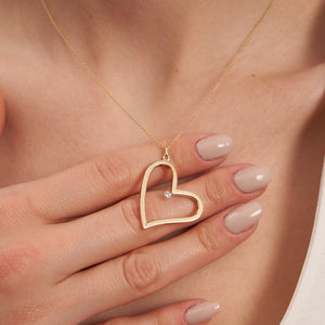 Introducing the 14K Solid Gold Large Open Heart Shaped Pendant Necklace, featuring a heart-shaped pendant adorned with a small diamond on one side. The elegant, slightly tilted heart hangs gracefully from a fine chain, making it an ideal gift for your girlfriend. It is beautifully showcased against a plain white background.