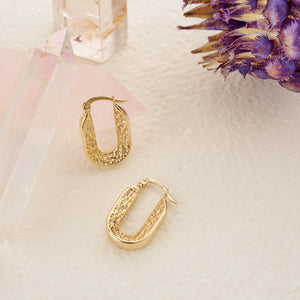 Displayed are two trendy 14K real gold hoop earrings featuring a chunky design. One earring showcases a smooth, solid side, while the other boasts an intricate texture. These elongated hoops are designed with a hinged closure at the top and are crafted to be hypoallergenic.