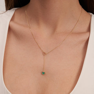 The 14K Solid Gold Heart Lariat Necklace features a sleek and elegant design, with a small heart-shaped malachite pendant at the end. The chain includes an interlocking heart design near the top, enhancing its overall intrigue.