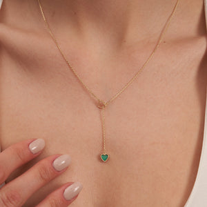 The 14K Solid Gold Heart Lariat Necklace features a sleek and elegant design, with a small heart-shaped malachite pendant at the end. The chain includes an interlocking heart design near the top, enhancing its overall intrigue.