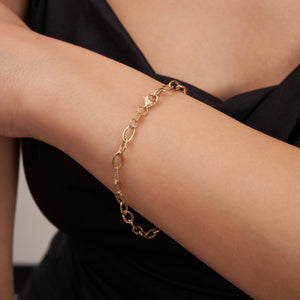 The 14K Gold Oval Paperclip Chain Bracelet is a delicate piece featuring oval links and a secure lobster clasp. Some of the links display a twisted texture, which adds subtle detail to the exquisite design of this women's gold jewelry.