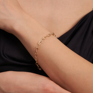 The 14K Gold Oval Paperclip Chain Bracelet is a delicate piece featuring oval links and a secure lobster clasp. Some of the links display a twisted texture, which adds subtle detail to the exquisite design of this women's gold jewelry.