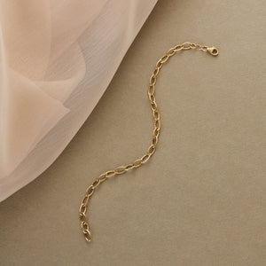 The 14K Gold Oval Paperclip Chain Bracelet is a delicate piece featuring oval links and a secure lobster clasp. Some of the links display a twisted texture, which adds subtle detail to the exquisite design of this women's gold jewelry.