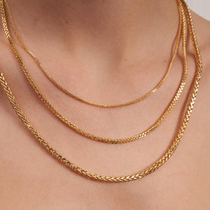 A close-up of the 14K Full Solid Gold Link Square Wheat Chain Necklace is displayed against a white background, showcasing its intricate diamond cut detailing. The necklace's shiny, polished finish highlights its elegant and sophisticated design.