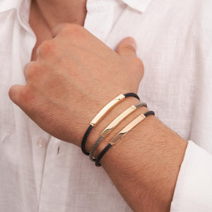 Introducing the 14K Solid Gold Nameplate ID Bracelet for Men, featuring a stylish design with a twisted black cable and a polished gold rectangular bar as the centerpiece. The gold-toned clasp is elegantly engraved with PRADA and 18Kt, adding a sleek and modern touch. This bracelet effortlessly enhances any men's jewelry collection.