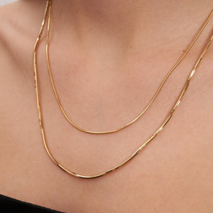 A 14K Solid Gold Round Snake Chain necklace is showcased against a white backdrop. Featuring an elegant design, this versatile layering piece offers a smooth and flexible look, subtly reflecting light across its polished surface.