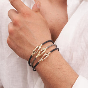 Introducing the 14K Solid Gold Knot Bracelet for Men, featuring a modern and elegant design with a sleek stainless steel bangle. It showcases a black twisted cable band accented by a central gold knot and is secured with a gold clasp.