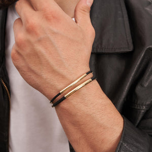 An elegant 14K Solid Gold Round Tube Nameplate ID Bracelet for men, showcasing a black braided band with a polished gold clasp and cylindrical accents. This minimalistic design merges elegance with simplicity, making it suitable for various occasions and perfect as a custom engraved bangle.