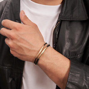 An elegant 14K Solid Gold Round Tube Nameplate ID Bracelet for men, showcasing a black braided band with a polished gold clasp and cylindrical accents. This minimalistic design merges elegance with simplicity, making it suitable for various occasions and perfect as a custom engraved bangle.