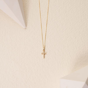 A refined necklace crafted from 14K solid gold features a small cross pendant adorned with genuine sparkling diamonds, displayed against a simple white background.