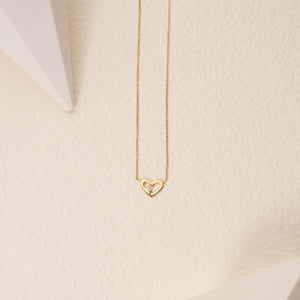 The Diamond Minimal Dainty Open Heart Necklace in 14K Solid Gold showcases a heart-shaped pendant adorned with a central diamond, gracefully suspended from a fine chain. Its delicate beauty is enhanced by the simplicity of the plain white background.