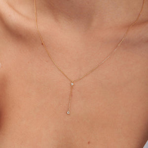 Introducing the 14K Solid Gold Diamond Lariat Y Necklace: This elegant piece showcases a delicate drop design, with two small natural diamonds encased in gold bezels. The diamonds are linked by a fine gold chain, creating a simple yet sophisticated appearance. The pendant is designed to hang vertically at the center.