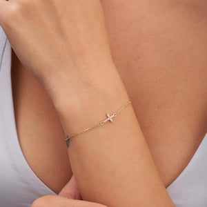 The 14K Solid Gold Tiny Diamond Cross Bracelet for Women showcases a refined design with a small horizontal cross charm embellished with delicate, sparkling stones, all linked by a slender chain and secured with a spring ring clasp.