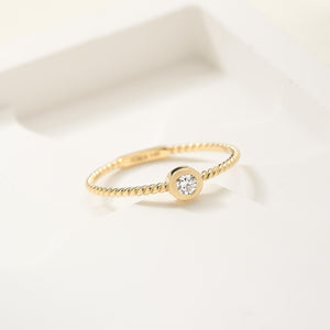 A 14K solid gold wedding band features a natural 0.11ct diamond in a bezel setting with a delicate braided design that highlights its simplicity and elegance.