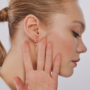 Displayed are two exquisite gold earrings: a pair of 14K Gold Clover Hoop Earrings and a uniquely designed earring shaped like a gingerbread man, complete with arms and legs and a top clasp for wearing. Both pieces boast a shiny, polished finish and make for an exceptional unique jewelry gift.