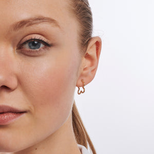 Displayed are two exquisite gold earrings: a pair of 14K Gold Clover Hoop Earrings and a uniquely designed earring shaped like a gingerbread man, complete with arms and legs and a top clasp for wearing. Both pieces boast a shiny, polished finish and make for an exceptional unique jewelry gift.